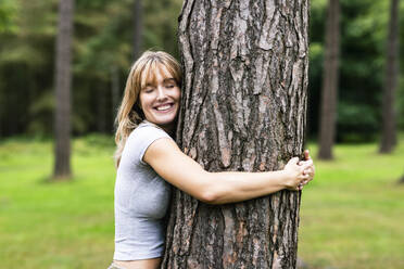 Smiling young beautiful woman hugging tree in forest - WPEF08288