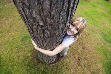 Smiling beautiful woman hugging tree - WPEF08301