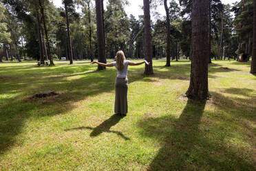 Frau steht mit ausgestreckten Armen im Wald an einem sonnigen Tag - WPEF08302