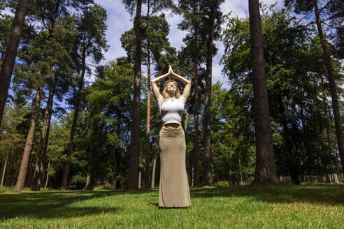 Lächelnde Frau mit verschränkten Händen vor einem Baum an einem sonnigen Tag - WPEF08307
