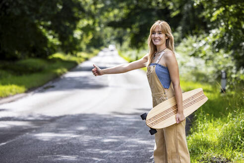 Glückliche Frau, die im Wald ein Skateboard in der Hand hält - WPEF08320