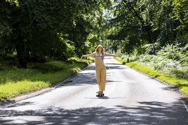 Young woman with arms outstretched skateboarding in forest - WPEF08324