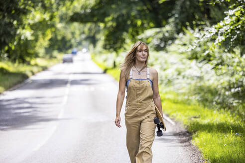 Young woman walking with skateboard in forest - WPEF08326