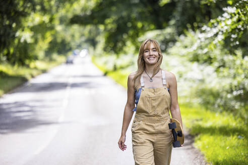 Happy woman walking with skateboard in forest - WPEF08327