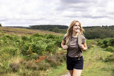 Lächelnde junge Frau geht mit Rucksack im Wald spazieren - WPEF08339