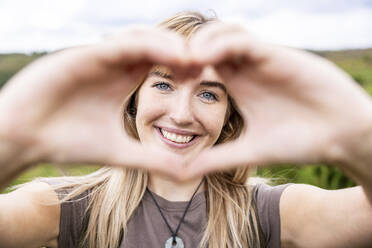 Happy young woman gesturing heart shape - WPEF08345