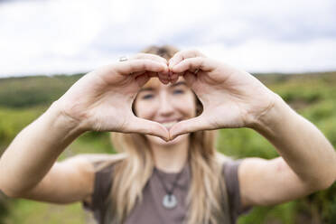 Young woman gesturing heart shape in forest - WPEF08346