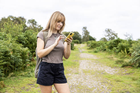 Lächelnde blonde Frau mit Smartphone im Wald - WPEF08349