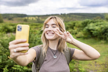 Glückliche blonde Frau nimmt Selfie durch Smartphone im Wald - WPEF08350