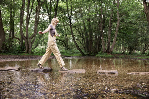 Junge Frau geht auf Felsen im Fluss - WPEF08353