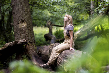 Thoughtful woman sitting on tree trunk in forest - WPEF08368