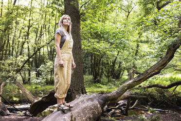 Frau steht auf einem Baumstamm im Wald - WPEF08372