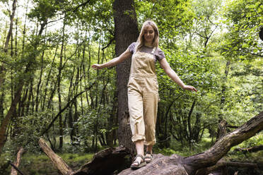 Blonde Frau geht auf einem Baumstamm im Wald - WPEF08375