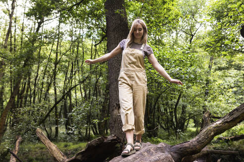 Blond woman walking on tree trunk in forest - WPEF08375