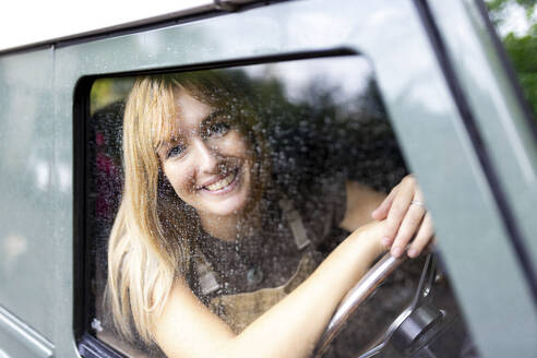 Smiling young woman sitting in car - WPEF08378