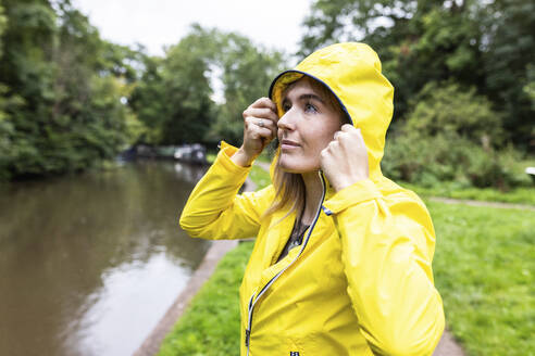 Junge Frau in gelber Jacke steht in der Nähe eines Flusses - WPEF08379