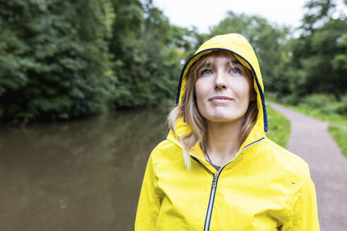 Smiling woman wearing yellow raincoat in forest - WPEF08381