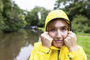 Smiling young woman wearing yellow raincoat in forest - WPEF08382