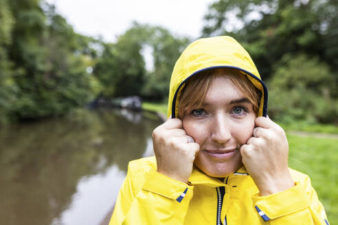 Lächelnde junge Frau in gelbem Regenmantel im Wald - WPEF08382