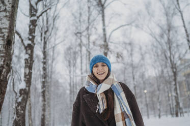 Smiling mature woman wearing warm clothes at snow park - ANAF02710