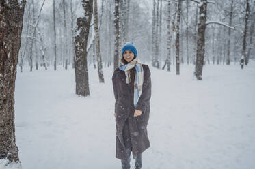 Smiling woman standing near trees at snow park - ANAF02711