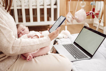 Freiberufler mit Smartphone und schlafendem Baby in der Nähe des Laptops zu Hause - EBBF08397