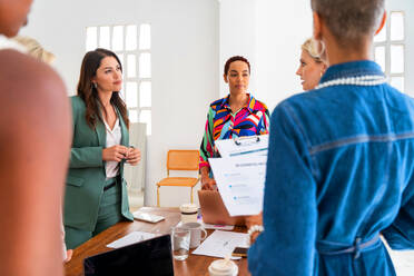 Group of beautiful confident businesswomen meeting in the office - Multiethinc female creative team brainstorming at work - Diverse colleagues working together in workshop in a co-working space - DMDF09655