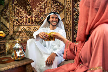 Junges Paar aus den Emiraten verbringt Zeit in einem traditionellen arabischen Café. Mann und Frau mit Kandura und Abaya aus Dubai unterhalten sich. - DMDF09715