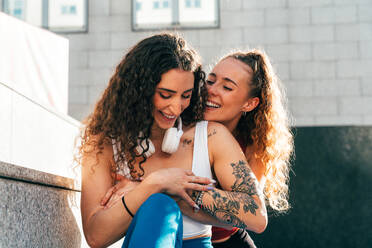 Two women in fitness wear hugging each other standing on rooftop