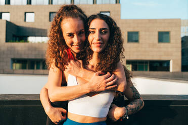 Two women in fitness wear hugging each other standing on rooftop