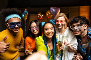 Eine Gruppe von Freunden feiert zu Hause am Neujahrsabend. Junge Frauen und Männer feiern in der Wohnung, trinken und essen, tanzen und haben Spaß. Konzept über Feiertage und Partys. - DMDF09879