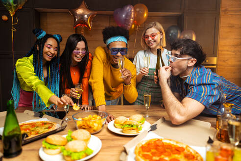 Eine Gruppe von Freunden feiert zu Hause am Neujahrsabend. Junge Frauen und Männer feiern in der Wohnung, trinken und essen, tanzen und haben Spaß. Konzept über Feiertage und Partys. - DMDF09881