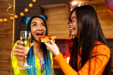 Eine Gruppe von Freunden feiert zu Hause am Neujahrsabend. Junge Frauen und Männer feiern in der Wohnung, trinken und essen, tanzen und haben Spaß. Konzept über Feiertage und Partys. - DMDF09883