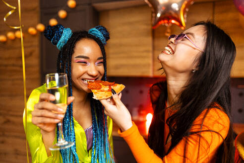 Eine Gruppe von Freunden feiert zu Hause am Neujahrsabend. Junge Frauen und Männer feiern in der Wohnung, trinken und essen, tanzen und haben Spaß. Konzept über Feiertage und Partys. - DMDF09884