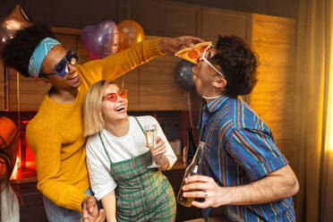 Eine Gruppe von Freunden feiert zu Hause am Neujahrsabend. Junge Frauen und Männer feiern in der Wohnung, trinken und essen, tanzen und haben Spaß. Konzept über Feiertage und Partys. - DMDF09885