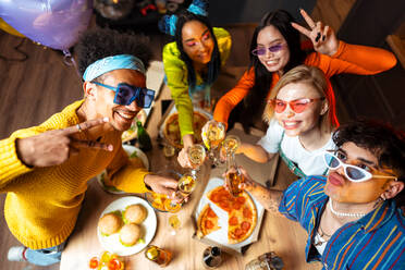 Eine Gruppe von Freunden feiert zu Hause am Neujahrsabend. Junge Frauen und Männer feiern in der Wohnung, trinken und essen, tanzen und haben Spaß. Konzept über Feiertage und Partys. - DMDF09894