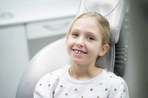 Lächelndes Mädchen sitzt auf dem Zahnarztstuhl in der Klinik - NJAF00760