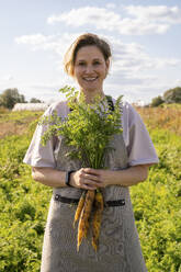 Lächelnder Landwirt mit einem Bündel Bio-Karotten auf einem Bauernhof - VPIF09272