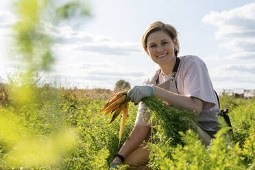 Smiling farmer holding carrots and crouching in farm - VPIF09275
