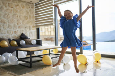 Glückliches Mädchen, das mit erhobenen Armen durch Luftballons auf dem Boden einer Villa springt - ANNF00808