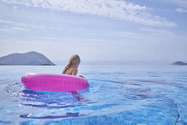 Girl swimming with inflatable tube in blue pool - ANNF00810