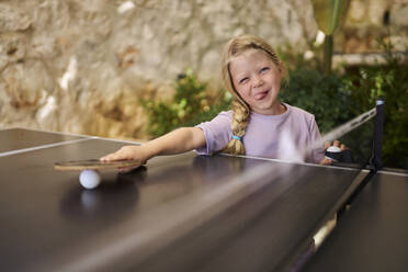 Verspieltes Mädchen streckt die Zunge heraus und hält einen Tischtennisschläger in einer Villa - ANNF00817