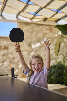 Glückliches Mädchen jubelt mit Tischtennisschläger und Ball in einer Villa - ANNF00818