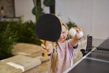 Lächelndes Mädchen zeigt Tischtennisschläger und Ball in einer Villa - ANNF00820