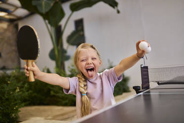 Unbekümmertes Mädchen hält Tischtennisschläger und Ball in einer Villa - ANNF00821