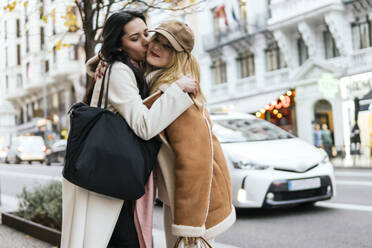 Young woman embracing and kissing friend standing at street in city - PBTF00424