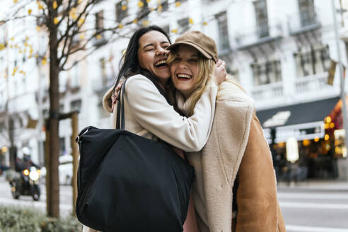 Happy woman laughing with friend standing at street in city - PBTF00425