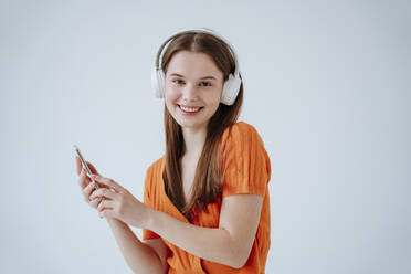 Lächelnde Frau, die über drahtlose Kopfhörer vor einem weißen Hintergrund Musik hört - NLAF00240