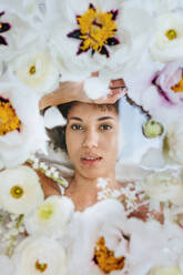 Young woman lying under glass surface with flowers - YTF01692