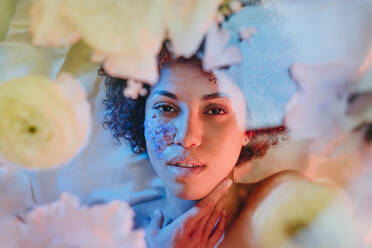 Beautiful woman lying behind glass surface with flowers under neon lights - YTF01698